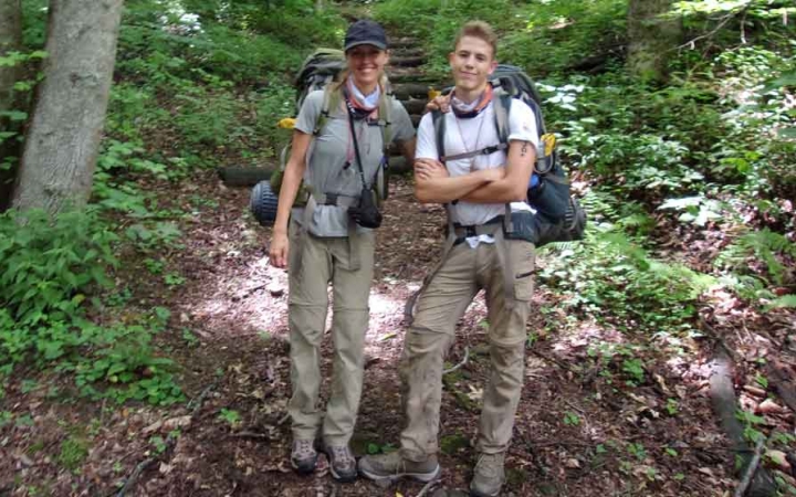 a parent and their child are wearing backpacking gear while smiling at the camera on an outward bound course in north carolina